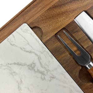 A marble cheeseboard with a wood base, accompanied by a metal cheese knife and fork.