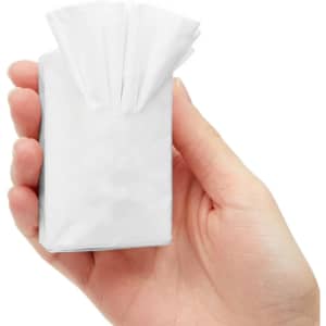 A hand holding a small, white packet of tissues with multiple tissues protruding from the top.