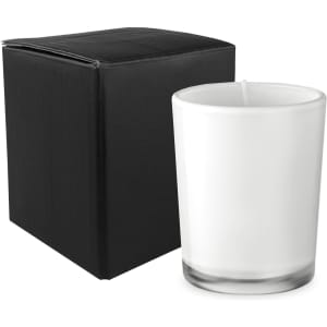 A glass candle in a clear container next to a black box. The candle is white and has a simple design.