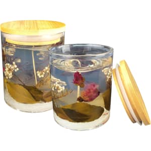 A floral candle in a glass jar with a wooden lid, featuring preserved flowers and leaves in clear wax.