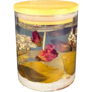 A floral candle in a clear jar featuring dried flowers and leaves, topped with a bamboo lid.