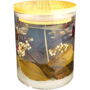 A floral candle in a clear glass jar, featuring dried flowers and leaves, topped with a bamboo lid.