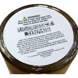 A floral candle in a glass container with a warning label on the base, featuring earthy tones and a subtle design.