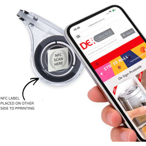 A correction tape dispenser in clear plastic, with a black tape inside, next to a smartphone displaying a website.