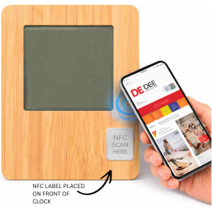 A bamboo desk clock featuring a grey display, with an NFC label and a hand holding a smartphone nearby.