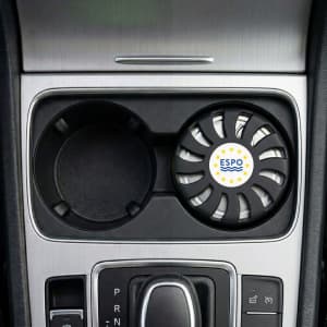 An air freshener in a circular black holder, placed in a car cup holder, featuring a logo.