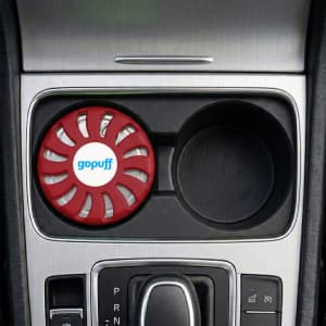 A red air freshener sits in a car cup holder, featuring a logo on the front.