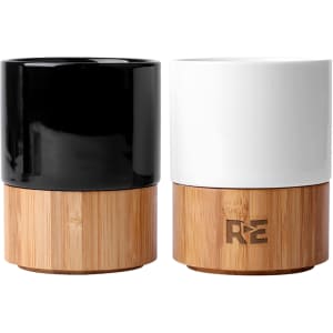 A pair of ceramic mugs in black and white, featuring a bamboo base and a logo.
