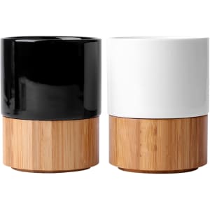 A pair of ceramic mugs featuring a black and a white glossy finish, both with bamboo bases. Each has a branding logo.