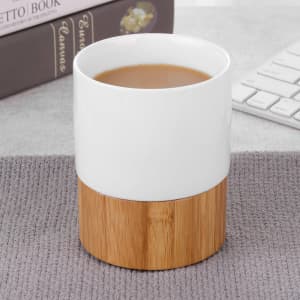 A ceramic mug with a white upper section and a natural bamboo base, filled with a warm beverage.