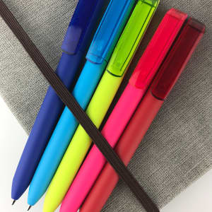 Five plastic pens in blue, green, yellow, pink, and red, arranged on a grey notebook and secured with an elastic band.