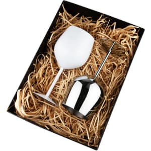 A stainless steel wine glass and a white wine glass displayed in a black box with straw filler. The box has a logo.