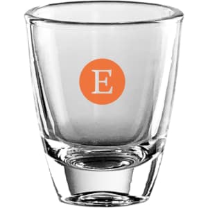 A clear glass shot glass with a solid base and an orange circular logo containing the letter "E."