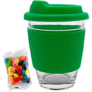 A glass coffee cup with a green silicone lid and sleeve, accompanied by a pack of colourful jelly beans.