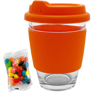 A clear glass coffee cup with an orange silicone sleeve and lid, accompanied by a pack of colourful jelly beans.