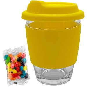 A glass coffee cup with a yellow silicone lid and sleeve, accompanied by a packet of colourful jelly beans.