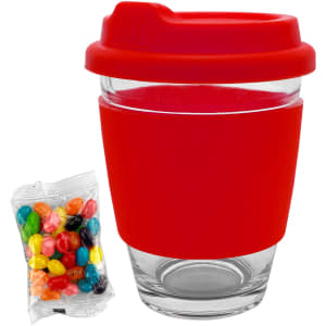 A glass coffee cup with a red silicone lid and sleeve, accompanied by a pack of colourful jelly beans.