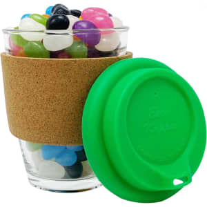 A clear glass coffee cup with a cork band and a green silicone lid, filled with colourful jelly beans.