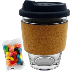 A glass coffee cup with a black lid and cork band, accompanied by a packet of colourful jelly beans.