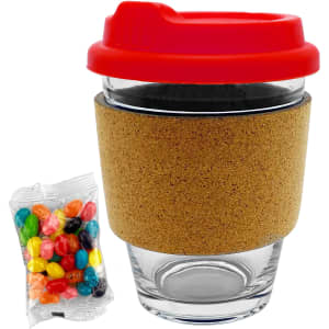 A glass coffee cup with a cork band and a red lid, accompanied by a pack of colourful jelly beans.