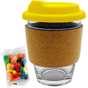 A glass coffee cup with a cork band and a yellow lid, accompanied by a pack of colourful jelly beans.