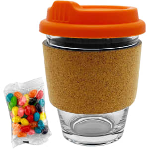 A glass coffee cup with an orange lid and cork band, accompanied by a bag of colourful jelly beans.