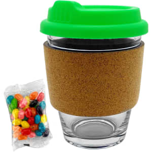 A glass coffee cup with a cork band and a bright green lid, accompanied by a pack of colourful jelly beans.