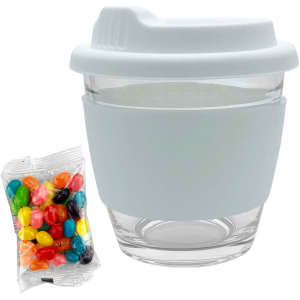 A reusable glass coffee cup in white with a silicone sleeve, accompanied by a bag of colourful jelly beans.