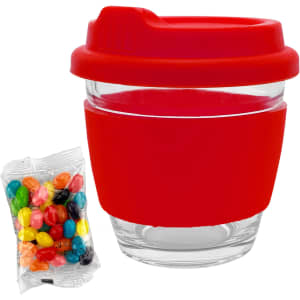 A reusable glass coffee cup with a red silicone lid and sleeve, alongside a packet of colourful jelly beans.
