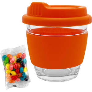 A glass coffee cup with an orange silicone lid and sleeve, accompanied by a pack of colourful jelly beans.
