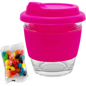 A reusable glass coffee cup with a bright pink silicone lid and sleeve, alongside a packet of multi-coloured jelly beans.