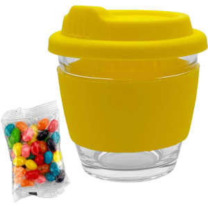 A yellow glass coffee cup with a silicone sleeve and lid, alongside a packet of colourful jelly beans.