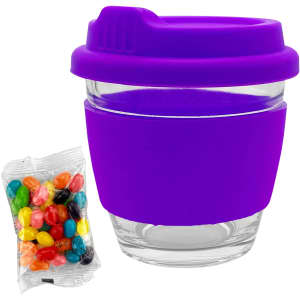 A reusable coffee cup featuring a clear glass body and a vibrant purple silicone sleeve and lid, alongside a bag of jelly beans.