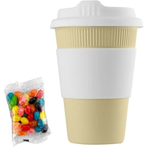 A reusable 12oz bamboo coffee cup in light beige with a white silicone sleeve, alongside a bag of colourful jelly beans.