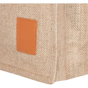 A jute bag in a natural beige colour features a tan leather patch, showcasing a simple and eco-friendly design.