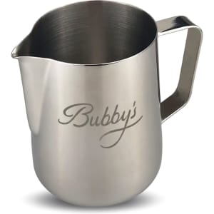 A stainless steel milk jug with a polished finish and a curved handle, featuring a logo on the side.