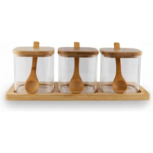 Three glass condiment jars with bamboo lids and wooden spoons, placed on a bamboo tray.