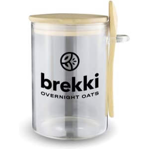 A clear overnight oats container with a wooden lid and spoon, featuring a logo on the side.