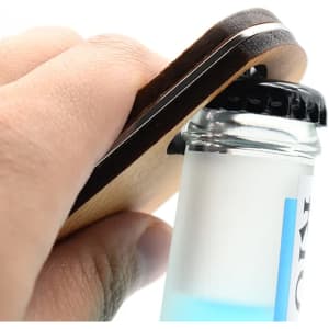 A drink bottle opener key ring made of bamboo, being used to open a glass bottle with a black cap.