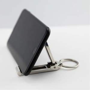 A black phone propped up by a silver mobile stand and hanger key ring, showcasing its compact design.