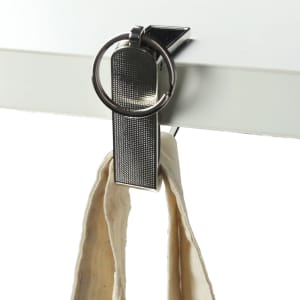 A silver mobile stand and hanger key ring clipped to a flat surface, holding a fabric strap.