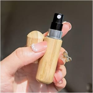 A small bamboo atomiser held in a hand, featuring a silver nozzle and a matching bamboo cap.