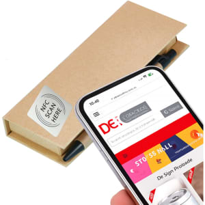 A cream-coloured box with a pen, featuring an NFC tag, sits next to a smartphone displaying a website.