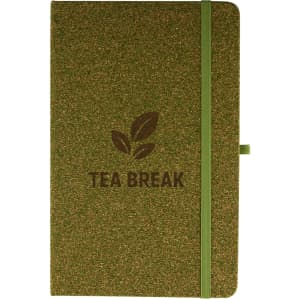 A green cork notebook with a matching elastic band and a logo featuring tea leaves.
