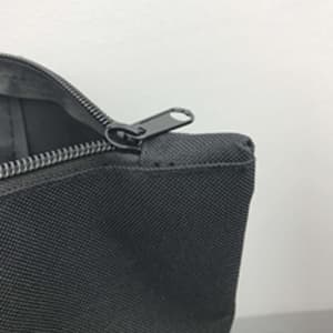 A grey nylon tote bag featuring a zipper closure and a metal zipper pull. It has a simple, minimalist design.