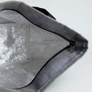 A grey lunch bag with a silver insulated interior and a zip closure, featuring a black handle.