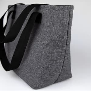 A grey lunch bag with black straps, featuring a simple design and an external logo.