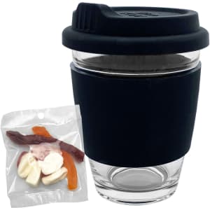 A reusable clear glass coffee cup with a black silicone sleeve beside a packet of jelly sweets.