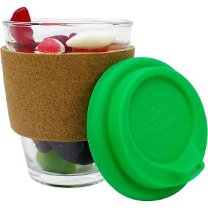 A glass coffee cup filled with mixed lollies, featuring a cork band and a green silicone lid.
