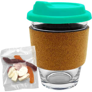 A glass coffee cup with a cork band and a teal lid, accompanied by a pack of mixed lollies in various colours.